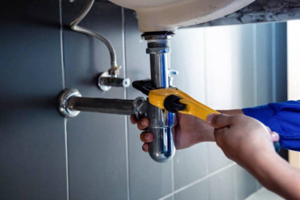 Plumber fixing white sink pipe with adjustable wrench.
